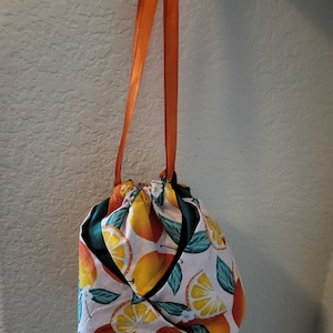 May include: A small drawstring bag with orange straps. The bag is made of fabric with a white background and a pattern of orange and yellow lemons and green leaves.