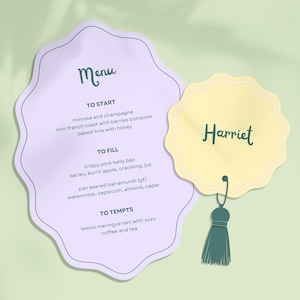 May include: A light purple scalloped menu card with dark green text listing courses including mimosa, french toast, pork belly, and barramundi, paired with a smaller yellow scalloped name tag labeled Harriet featuring a dark green hanging tassel.