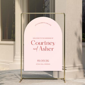 May include: A pink wedding welcome sign with a gold arch design. The sign reads "Let's celebrate our love. Welcome to the wedding of Courtney and Asher. 19.09.26 Athol Hall, Mosman."