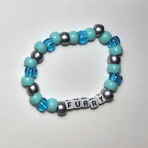 May include: Four colourful beaded bracelets. One is pink and red, another is green and blue, a third is brown and yellow with cat face beads, and the last is blue and silver. Each bracelet spells "FURRY" with letter beads.