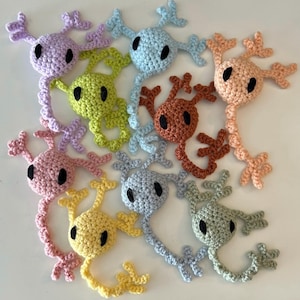 May include: A collection of ten crocheted amigurumi creatures in various colours, including light blue, light pink, light green, yellow, brown, and grey. Each creature has a round head with black eyes and a long, segmented body.
