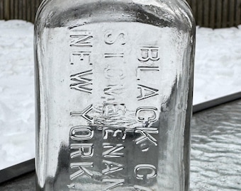 May include: Clear glass bottle with embossed text: "BLACK & GAY, STOWE, N.Y." and "NEW YORK". The bottle has a rectangular shape with rounded shoulders and a short neck. The background shows a snowy outdoor scene.