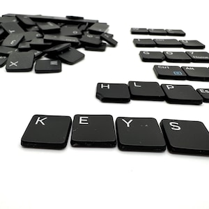 May include: Black keyboard keys spelling out the word "KEYS" with additional keys scattered around. The keys are arranged in a line with the word "HELP" spelled out above the word "KEYS".