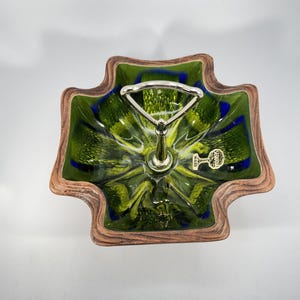 May include: A decorative serving dish with a green and blue floral design. The dish has a brown, wood-like border and a silver handle. The label reads "SEDDONIA WARE".