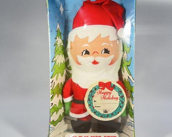 May include: A Knickerbocker Holiday Miniatures Santa Claus doll in its original packaging. The plush Santa wears a red suit with a matching hat, black boots, and green mittens. A circular gift tag with a wreath graphic reads Happy Holiday.