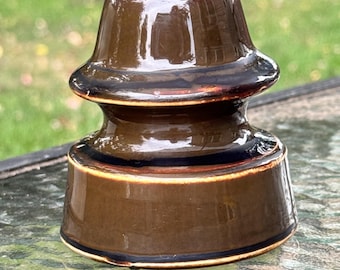 May include: A brown ceramic insulator with a glossy finish. The antique piece has a rounded top and a cylindrical base, with dark brown and black accents. The insulator is likely from an electrical or telephone system.