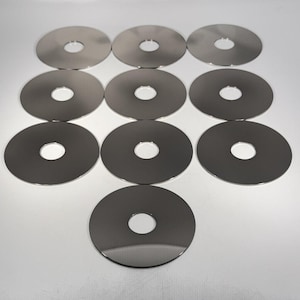 Peut inclure: Dix disques métalliques circulaires identiques disposés en grille. Chaque disque présente une surface argentée lisse et réfléchissante avec une découpe circulaire centrale. Les objets sont placés sur une surface unie et claire, avec une finition uniforme.
