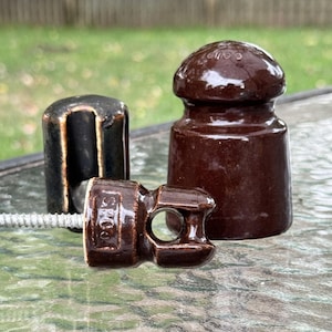May include: Three antique brown ceramic insulators of varying shapes and sizes. One is cylindrical, one is mushroom-shaped, and the third has the text "SECO" on it. A metal rod is attached to one of the insulators.