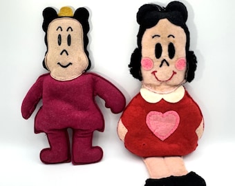 May include: Two handmade felt dolls. One doll is wearing a burgundy dress and has black hair with a gold crown. The other doll is wearing a red dress with a pink heart and has black hair with pink cheeks.