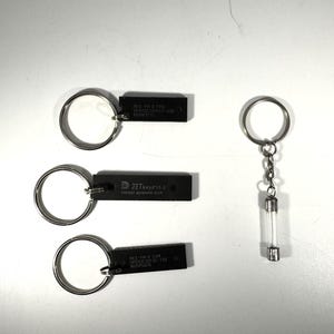 Puede incluir: Tres llaveros negros con anillos plateados. Dos tienen etiquetas rectangulares negras con texto, incluyendo "JETkeys v1.0 FASTEST KEYBOARD BUCK". El tercer llavero tiene un tubo de vidrio transparente con extremos metálicos.