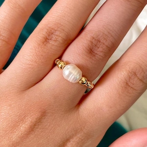 May include: A gold ring with a single white pearl bead. The ring is made of small gold beads.
