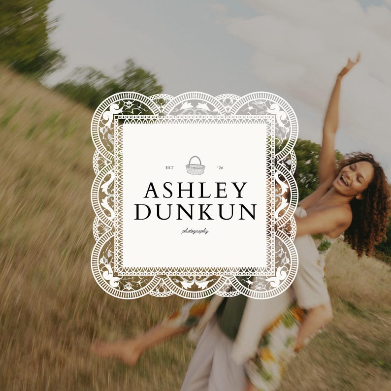 May include: A logo with a decorative border and the text "ASHLEY DUNKUN photography." The logo includes a basket illustration and the text "EST '26". The background features a blurred image of a person outdoors.