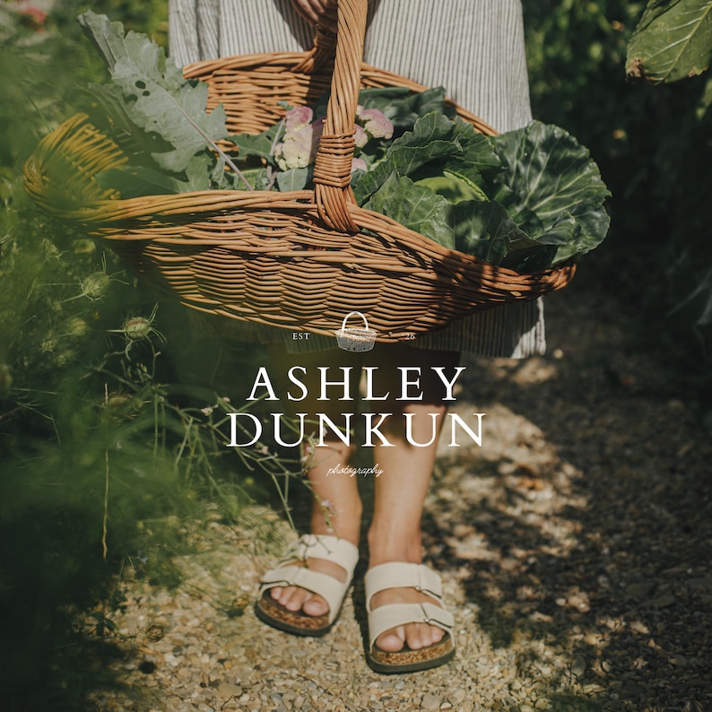 May include: A person holding a woven wicker basket filled with fresh green vegetables and flowers. The basket has a sturdy handle and is being carried outdoors. The image includes the text "ASHLEY DUNKUN photography". The person is wearing white sandals.