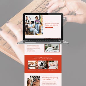 May include: A silver laptop displaying a website with the text "I help YOU keep your business in ORDER!" and "Ways to Work Together." The website features images of people and text. The laptop is on a wooden surface, with hands typing on a keyboard.