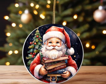 Könnte beinhalten: Runder Weihnachtsschmuck mit dem Weihnachtsmann in rotem Anzug und Mütze, der einen Stapel Bücher hält. Auf der linken Seite ist ein Weihnachtsbaum zu sehen. Der Schmuck hat eine goldene Schnur zum Aufhängen.
