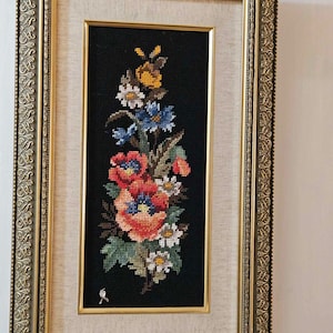 May include: A framed embroidery depicting a colorful floral arrangement with red, orange, yellow, blue, and white flowers on a black background.