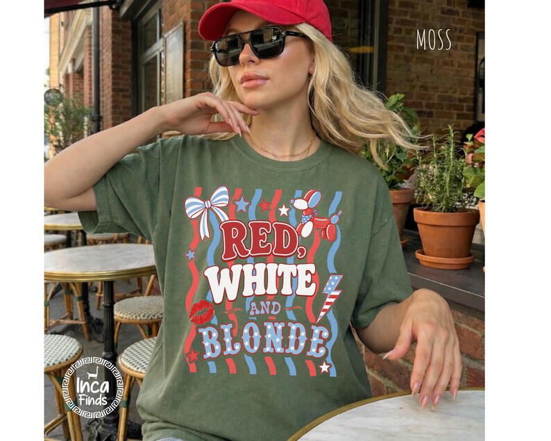 May include: Olive green t-shirt with the text "RED, WHITE, AND BLONDE" in red, white, and blue. The shirt features a bow, a balloon dog, a kiss, and an American flag graphic. The word "MOSS" is in the upper right corner.
