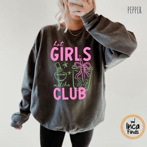 May include: Dark gray sweatshirt with the text "hot GIRLS matcha CLUB" in pink and green. The graphic includes a matcha bowl, whisk, and a matcha drink. The word "Pepper" is printed in black at the top right.