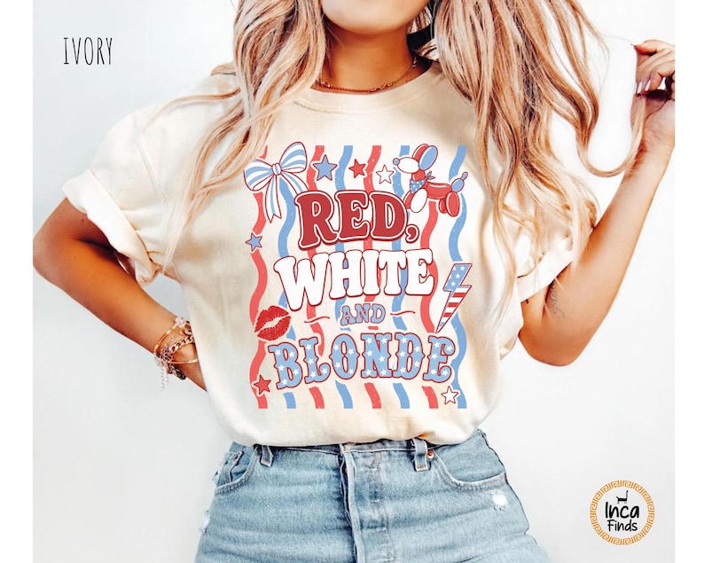 May include: Cream-coloured t-shirt featuring the text "RED, WHITE and BLONDE" in red, white, and blue. The design includes a bow, stars, a poodle balloon, a kiss, and a lightning bolt. The shirt is worn with blue denim shorts.