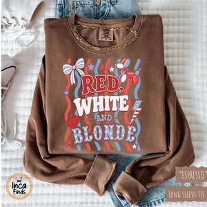 May include: A brown long-sleeve sweatshirt with the text "Red, White, and Blonde" in red, white, and blue. The design includes a bow, stars, a balloon dog, a kiss, and a lightning bolt. The sweatshirt is labeled "Espresso".