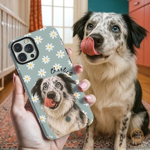 Könnte beinhalten: Hellblaue Handyhülle mit einem Hundepotrait mit blauen Augen und rosa Zunge, umgeben von weißen Gänseblümchen. Der Name "Charlie" steht auf der Hülle. Der Hund im Bild leckt sich die Nase.