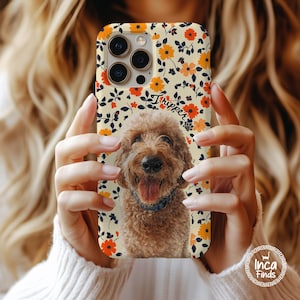 May include: A phone case featuring a cream background with a repeating pattern of orange and red flowers and dark blue leaves. The centre displays a realistic portrait of a brown curly-haired dog with its tongue out, wearing a blue collar.