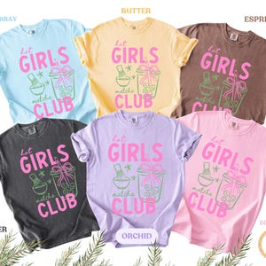 May include: A collection of six t-shirts in various colors, including blue, yellow, brown, black, purple, and pink. Each shirt features the text "Hot Girls Matcha Club" in pink and green, along with matcha-themed graphics.