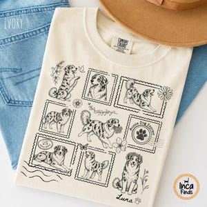 Könnte beinhalten: Ein elfenbeinfarbenes T-Shirt mit schwarzen Strichzeichnungen von Australian Shepherd Hunden in Briefmarkenrahmen. Das Design enthält florale Akzente, einen Pfotenabdruck-Stempel mit der Aufschrift Aussie Dog Express und den Text Luna.
