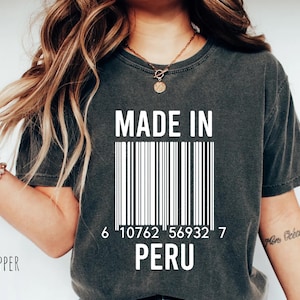 Peut inclure: T-shirt gris foncé avec l'inscription "MADE IN PERU" et un motif de code-barres blanc. Le t-shirt a un aspect vintage. Le texte et le code-barres sont blancs.