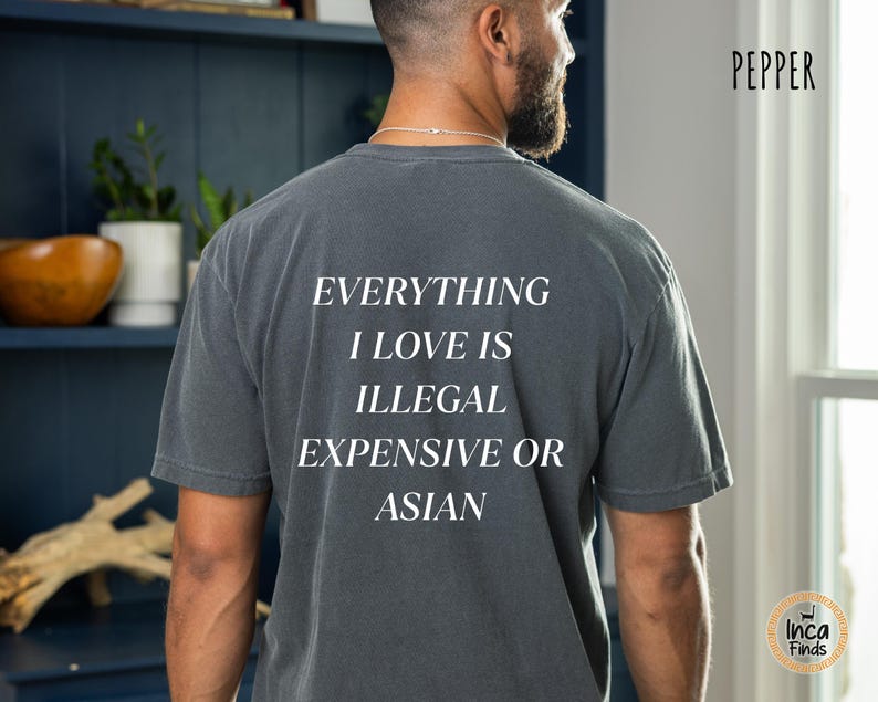 Op de afbeelding: Donkergrijs t-shirt met de witte tekst "EVERYTHING I LOVE IS ILLEGAL EXPENSIVE OR ASIAN". Het shirt heeft een relaxte pasvorm en korte mouwen. Het woord "Pepper" staat rechtsboven.