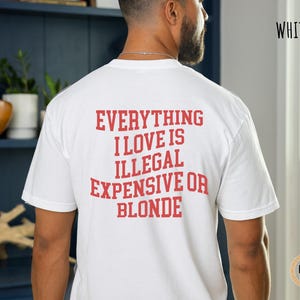 Pu&ograve; includere: T-shirt bianco con la scritta "EVERYTHING I LOVE IS ILLEGAL EXPENSIVE OR BLONDE" in lettere rosse. La maglietta &egrave; a girocollo.
