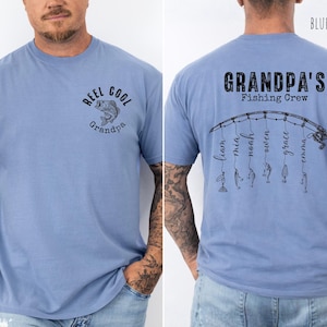 May include: A blue jean colored t-shirt featuring a front graphic of a fish with the text REEL COOL Grandpa. The back displays a fishing rod graphic with the text GRANDPA'S Fishing Crew and six names hanging from the line as fishing lures.