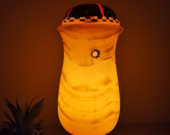 May include: A white alabaster lamp with a black and red patterned top. The lamp is lit and casting a warm glow.