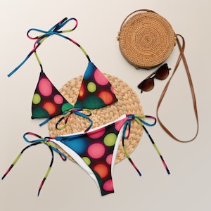 Könnte beinhalten: Ein farbenfroher Bikini mit einem leuchtenden, abstrakten Muster aus Kreisen in den Farben Pink, Grün, Blau und Orange. Das Bikinioberteil ist ein Dreiecksmodell mit verstellbaren Trägern. Das Bikiniunterteil ist ein freches Modell mit Bändern an den Seiten.