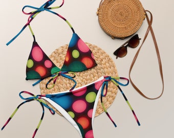 Könnte beinhalten: Ein farbenfroher Bikini mit einem leuchtenden, abstrakten Muster aus Kreisen in den Farben Pink, Grün, Blau und Orange. Das Bikinioberteil ist ein Dreiecksmodell mit verstellbaren Trägern. Das Bikiniunterteil ist ein freches Modell mit Bändern an den Seiten.