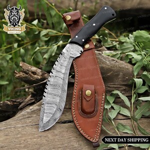 May include: A Damascus steel knife with a black handle and a brown leather sheath. The blade has a unique pattern and a serrated edge. The sheath has a button closure. The knife is designed for outdoor use.