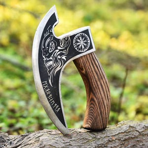 May include: A silver and black axe with a skull design and runic inscriptions on the blade. The axe has a wooden handle with a curved design. The blade features a decorative circular emblem. The axe is resting on a tree branch.