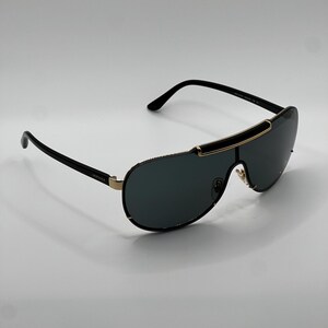 Peut inclure: Lunettes de soleil noires et dor&eacute;es avec des verres fonc&eacute;s. Les lunettes ont un design &eacute;l&eacute;gant et moderne avec une barre sup&eacute;rieure incurv&eacute;e et des branches fines. Le nom de la marque est visible sur la branche.