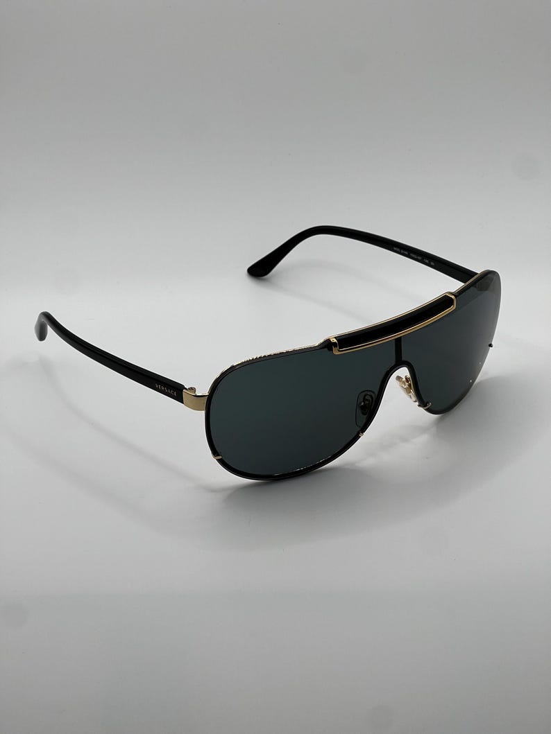 Peut inclure: Lunettes de soleil noires et dor&eacute;es avec des verres fonc&eacute;s. Les lunettes ont un design &eacute;l&eacute;gant et moderne avec une barre sup&eacute;rieure incurv&eacute;e et des branches fines. Le nom de la marque est visible sur la branche.
