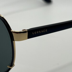 Peut inclure: Lunettes de soleil noires avec des d&eacute;tails dor&eacute;s et le nom de la marque "VERSACE" imprim&eacute; sur la branche. Les lunettes ont une forme aviateur classique avec des verres fonc&eacute;s et une monture dor&eacute;e.