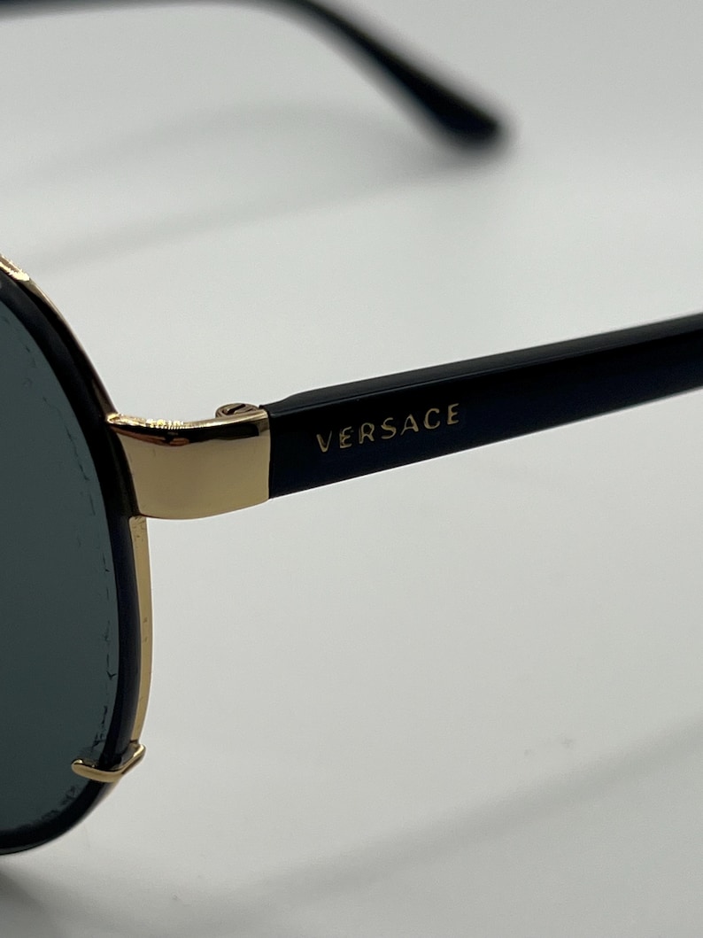 Peut inclure: Lunettes de soleil noires avec des d&eacute;tails dor&eacute;s et le nom de la marque "VERSACE" imprim&eacute; sur la branche. Les lunettes ont une forme aviateur classique avec des verres fonc&eacute;s et une monture dor&eacute;e.