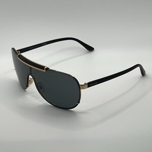 Peut inclure: Lunettes de soleil noires et dor&eacute;es avec un verre en forme d'&eacute;cran. Les lunettes ont une monture noire avec des accents dor&eacute;s et des verres fonc&eacute;s. Le nom de la marque "Versace" est visible sur la branche.