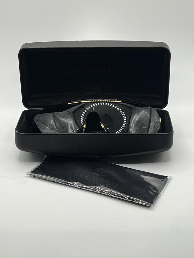 Peut inclure: Lunettes de soleil noires au design unique, pr&eacute;sent&eacute;es dans un &eacute;tui noir ouvert. Un chiffon de nettoyage est &eacute;galement visible. La marque "VERSACE" est visible sur l'&eacute;tui. Un accessoire de mode &eacute;l&eacute;gant.