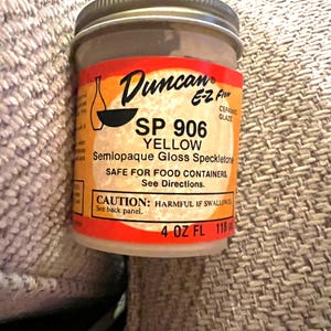 May include: A 4 ounce bottle of Duncan E-Z Flow ceramic glaze in yellow. The label reads "SP 906 Yellow Semiopaque Gloss Speckletone" and "Safe for food containers. See directions. Caution: Harmful if swallowed. See back panel."
