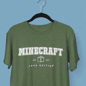 Peut inclure: Un t-shirt vert avec un logo Minecraft blanc et le texte "est. 2011 JAVA EDITION".