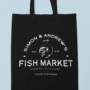 Può includere: Borsa tote nera con testo bianco che recita "Simon & Andrew's Family - Since 35 AD - Fish Market - "Freshest fish in the sea of Galilee" - Located in Bethsaida".