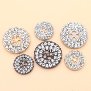 May include: Assortment of six round rhinestone buttons in various sizes. The buttons are silver, gold, and black with clear rhinestones.