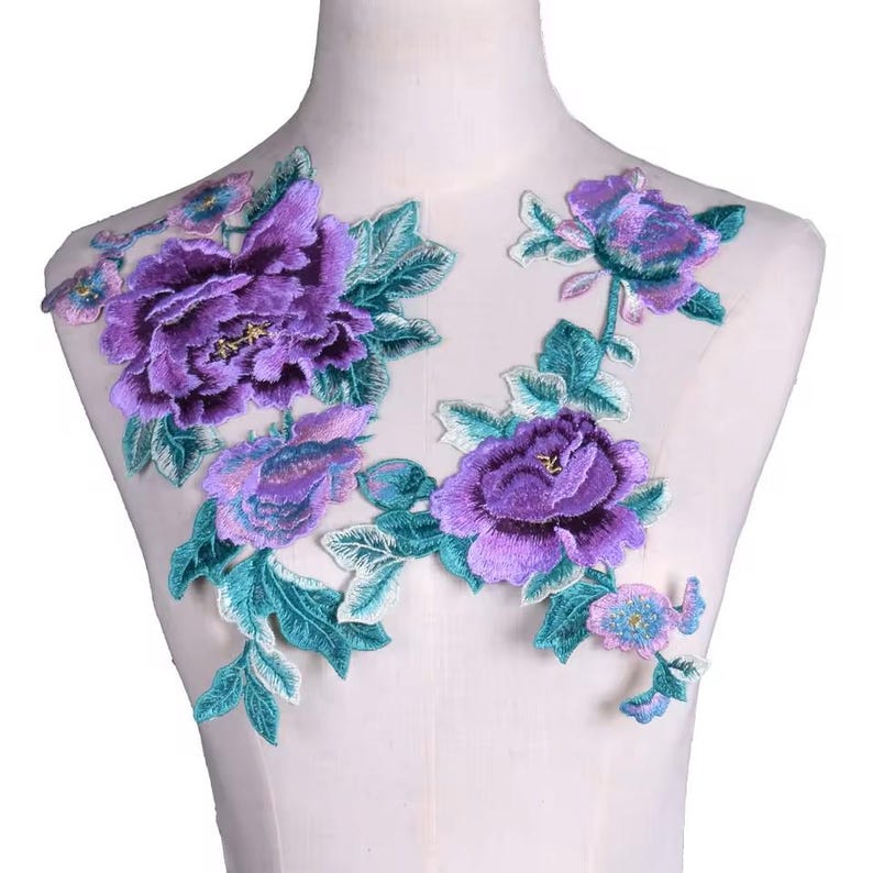 May include: Purple and teal floral embroidery applique with a delicate design. The applique features large peonies and smaller flowers with leaves.