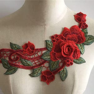 May include: Red and green embroidered floral applique with a delicate lace design. This applique features a large rose with smaller roses and leaves.