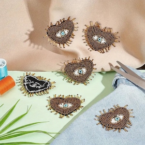 以下が含まれることがあります： 青と白の邪悪な目をデザインした、茶色のハート型のビーズパッチが6つ。パッチは薄い緑色の表面、茶色の表面、青いデニムの表面にあります。